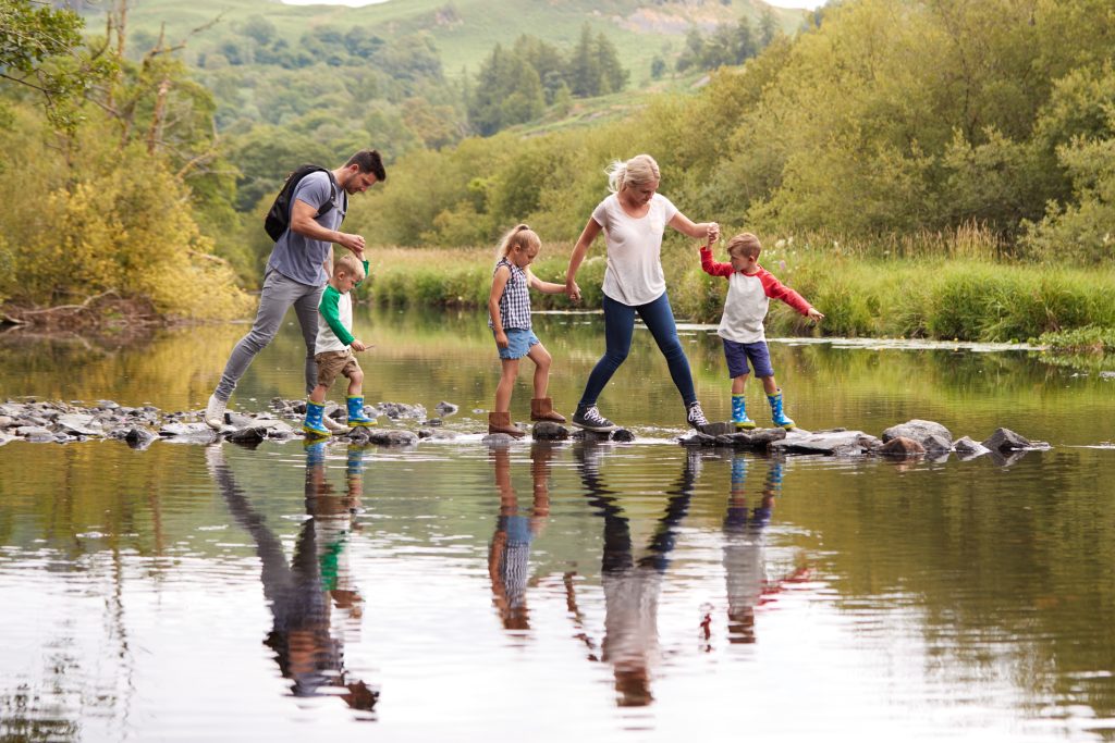 Family on holiday crossing river on stepping stones.